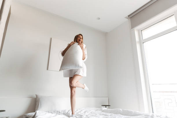 istock Happy pretty woman jumping with pillow 1325232050