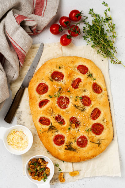 italienische traditionelle focaccia brot backen mit kirschroten tomaten, parmesan und rosmarin auf hellbraunem hintergrund. ansicht von oben - italian cuisine gluten free food tomato herb stock-fotos und bilder