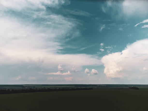 Aerial fly above green fields with stormy cloudscape. Dark rainy scenic heavy summer weather in rural agriculture area. Color graded