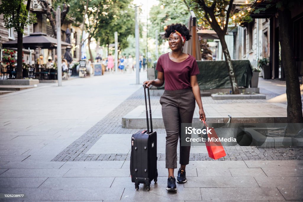 Young Afro woman arriving to the city and walking with her suitcase African American young female tourist walking through the city with her suitcase. Travel Stock Photo