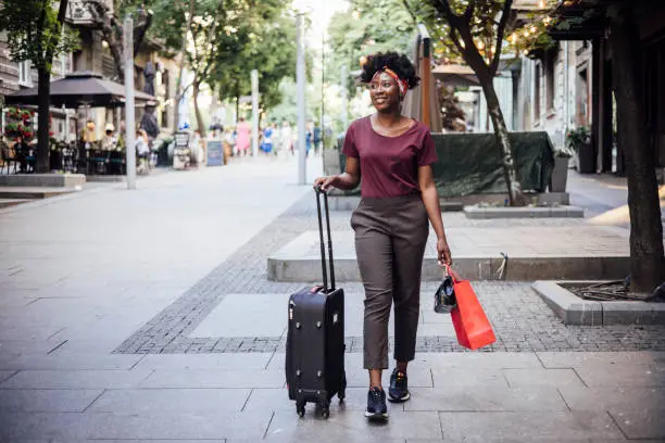 Photo of Young Afro woman arriving to the city and walking with her suitcase