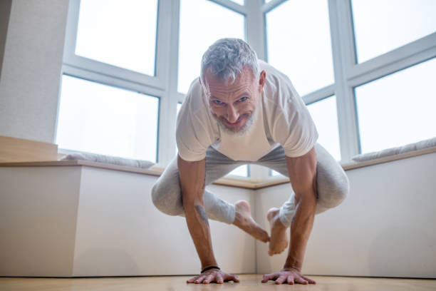 istock Gray-haired man in a white tshirt doing yoga and looking involved 1325240118