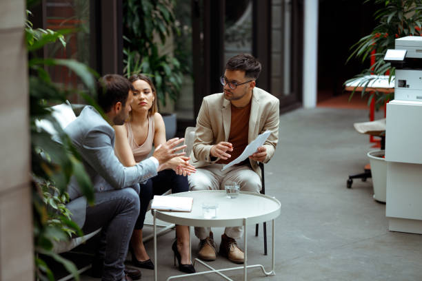 Business meeting Three colleagues are at a meeting in the foyer of the company's building. One of them is explaining new business strategies to the other two. georgijevic coworking stock pictures, royalty-free photos & images