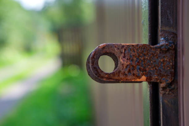 Rusty and stained gates against the background of a fence and dirt road stretching into the distance.