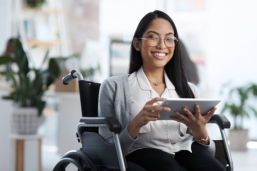Retrato recortado de una atractiva joven empresaria en silla de ruedas usando su tableta en la oficina photo