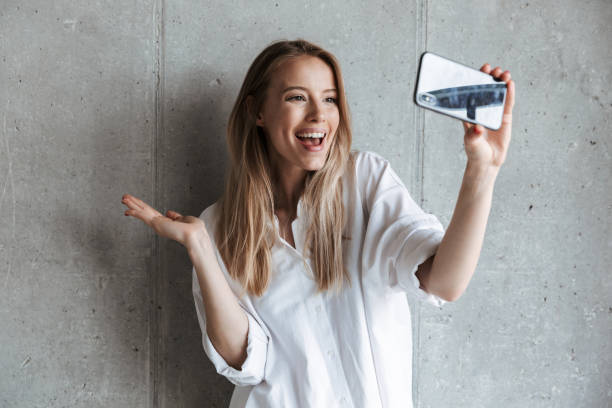 Portrait of a cheerful young girl taking a selfie Portrait of a cheerful young girl taking a selfie while standing over gray wall background selfie stock pictures, royalty-free photos & images