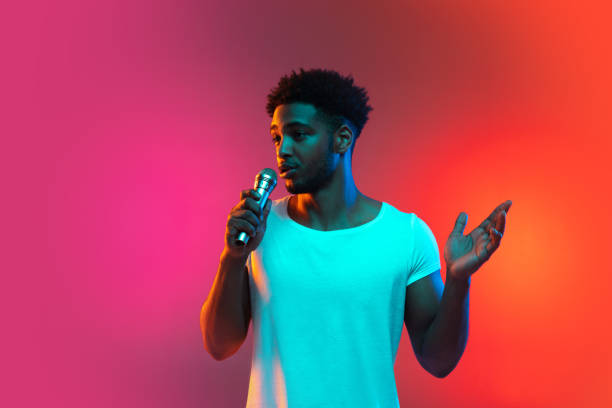 istock African American handsome young man singing into the microphone in the studio on a neon background. Music concept. 1325244681