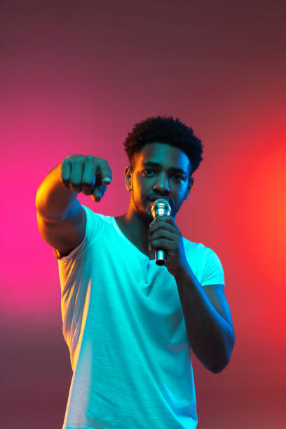 istock African American handsome young man singing into microphone in studio on neon background. Music concept. 1325244733