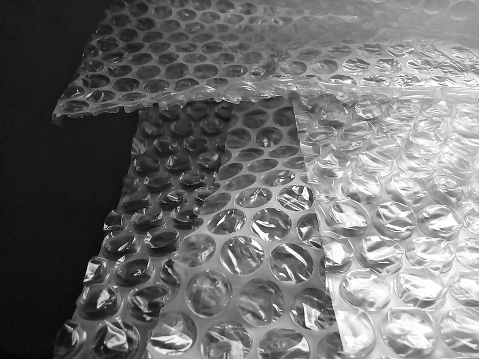 sheets of white bubble wrap on a dark background. plastic with air balls on the surface used for packing glassware or electronics or other sensitive items
