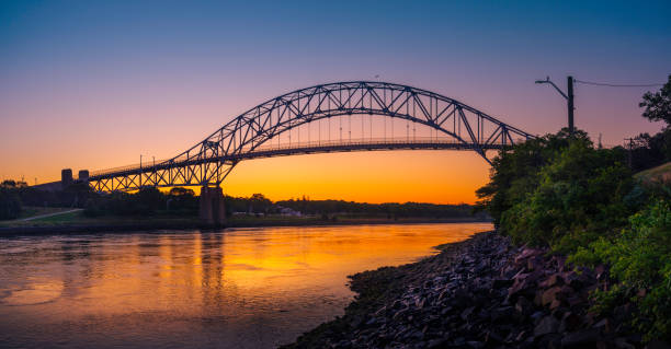 Sagamore Bridge Sunrise over Cape Cod Canal. Dawn Silhouette Architectural Image with Orange and Golden Colors. High Contrast Panoramic Seascape Image with Space for Text and Design.