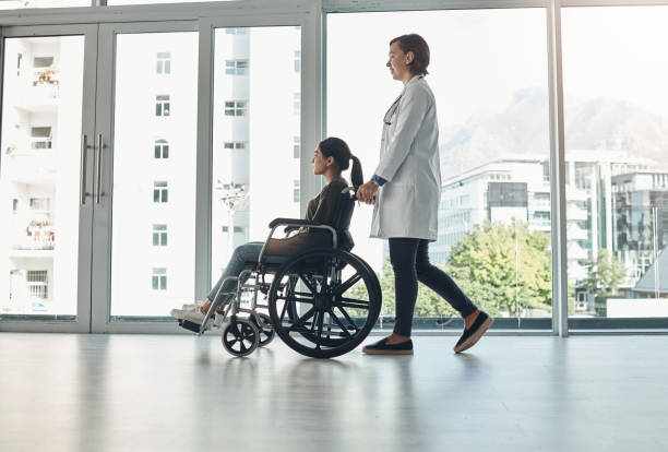 foto de una joven doctora empujando a un paciente en silla de ruedas en un hospital - desmovilización fotografías e imágenes de stock