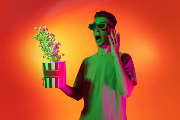 Portrait of Caucasian young man shouting with joy isolated on orange studio background in neon light. Concept of human emotions, facial expression. Movie, cinema. Excited happy young man with popcorn isolated on orange background in neon pink light. Handsome male model in casual style. Concept of emotions, facial expression. Copy space for ad. neon portrait boy stock pictures, royalty-free photos & images