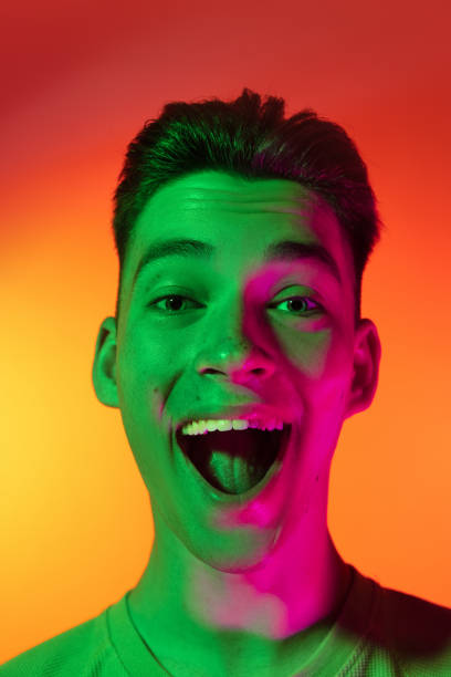 istock Close-up Caucasian young man shouting with joy isolated on orange studio background in neon light. Concept of human emotions, facial expression. Wow 1325250384