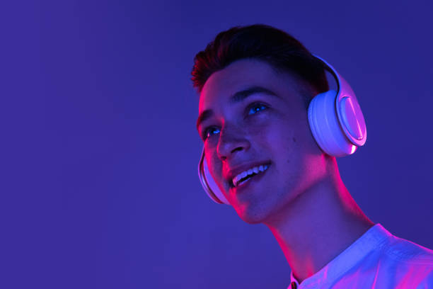 Caucasian young man in headphones isolated on blue studio background in neon light. Concept of human emotions, facial expression. Listening to music. Young man in headphones isolated on blue background in neon pink light. Handsome male model in casual style. Concept of human emotions, facial expression, youth. Copy space for ad. neon portrait boy stock pictures, royalty-free photos & images