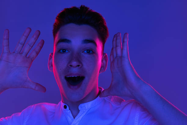 istock Close-up Caucasian young man shouting with joy isolated on orange studio background in neon light. Concept of human emotions, facial expression. Wow 1325250419