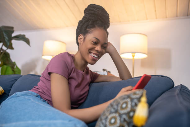 istock Cheerful darkskinned young woman with smartphone on sofa 1325250633