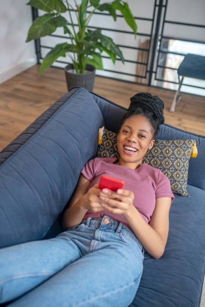 istock Smiling darkskinned woman with smartphone on sofa 1325251087