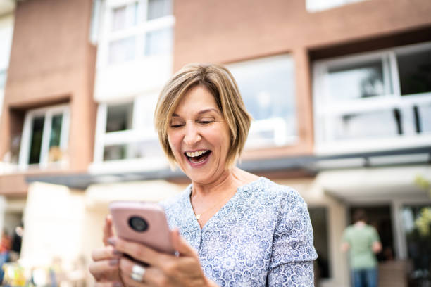 старшая женщина с помощью смартфона перед домом - lottery стоковые фото и изображения