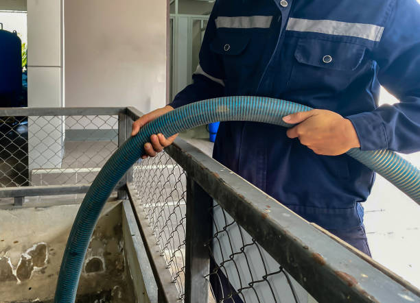 a worker wearing protective clothing holding a hose is pumping sludge out of a concrete sewage pond in a plant - sewage pond imagens e fotografias de stock