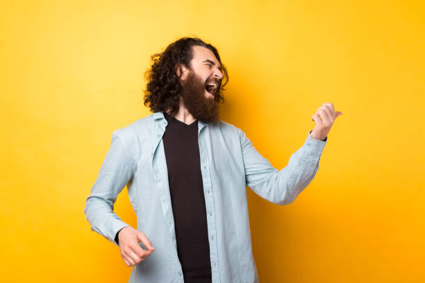 Photo of crazy bearded young man imitating playing guitar over yellow background Photo of crazy bearded young man imitating playing guitar over yellow background air guitar stock pictures, royalty-free photos & images