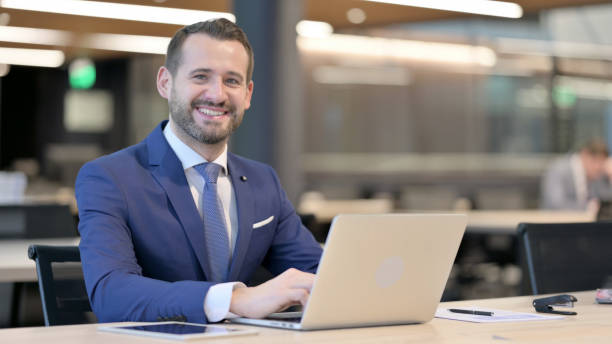 istock Middle Aged Businessman with Laptop Smiling at Camera 1325259101