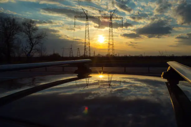 Power lines on the background of beautiful nature. Electric poles with wires are reflected on the roof of the car.