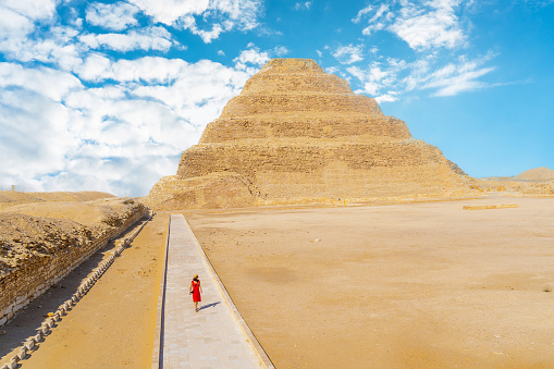 A young girl in a red dress walking in the Stepped Pyramid of Djoser, Saqqara. Egypt. The most important necropolis in Memphis. The first pyramid in the world