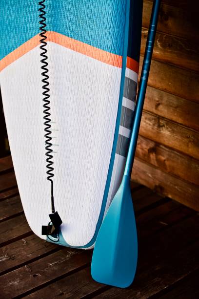 istock Paddleboard and surf board with paddle on brown wooden wall background close up 1325264706