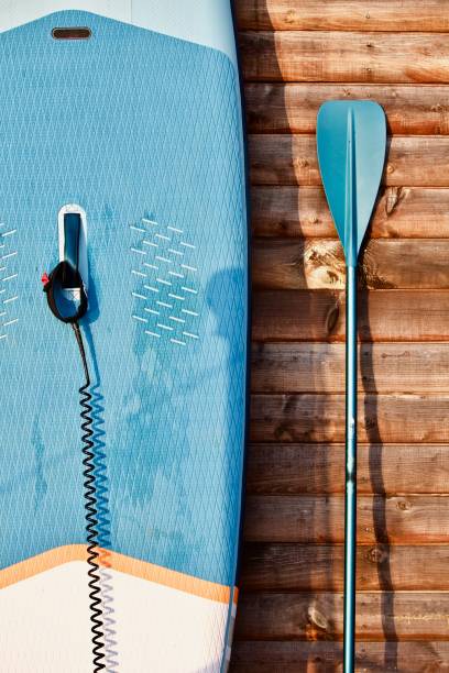 istock Paddleboard and surf board with paddle on brown wooden wall background close up 1325265043