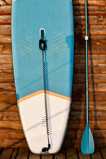 istock Paddleboard and surf board with paddle on brown wooden wall background close up 1325265256