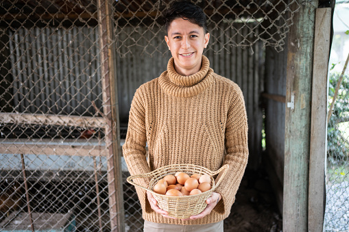 Happy young male poultry farm worker with a basket full of eggs. Male farmworker with eggs on the farm.