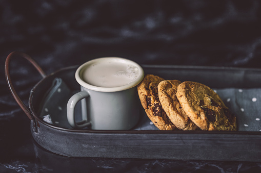 A plate of oatmeal cookies with chocolate and a glass of hot milk on a gray abstract background. Close-up.