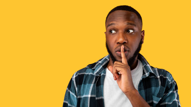 istock African american guy gesturing finger-on-lips looking aside over yellow background 1325274962