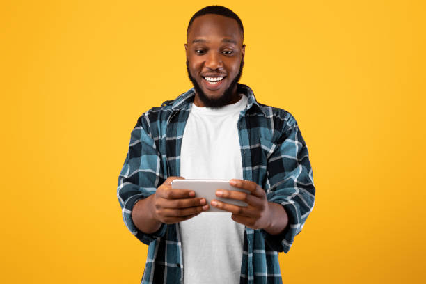 istock Happy Black Millennial Man Using Smartphone Playing Game, Yellow Background 1325275096