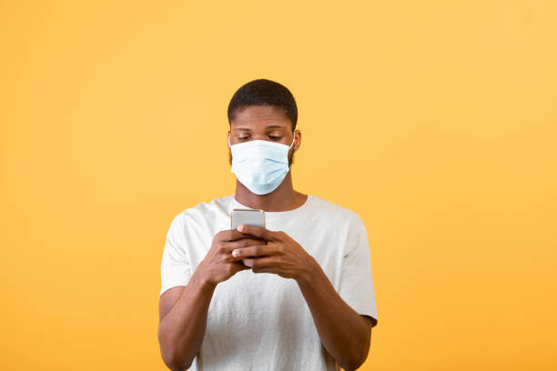 istock Self-isolation and social media during COVID-19 epidemic. Black man in protective mask using smartphone 1325278013