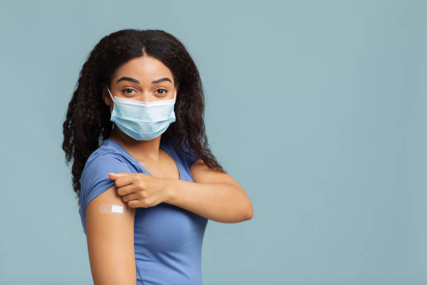 istock Antiviral immunization. Black lady vaccinated against covid-19, showing arm with plaster, standing on blue background 1325278544