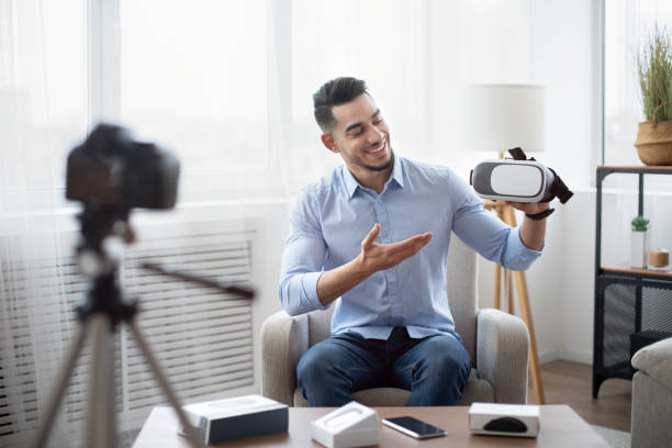 istock Tech product review. Male vlogger presenting VR headset, recording video about innovative device for technology blog 1325278817