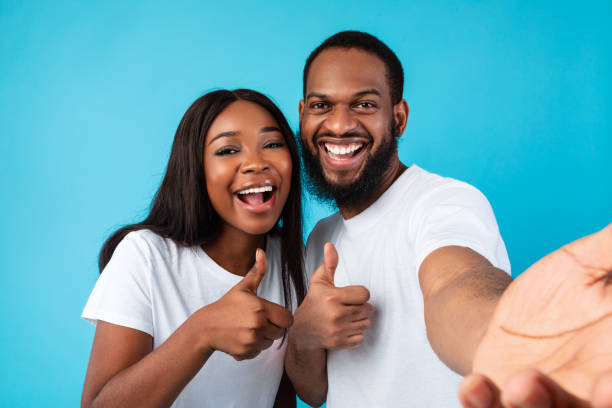 istock Happy afro couple taking selfie gesturing thumbs up and smiling 1325279636
