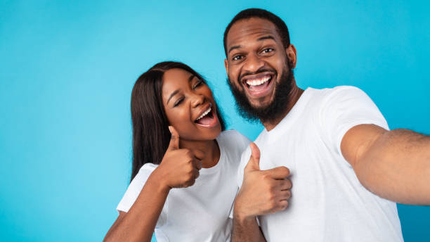 feliz pareja afro tomando selfie gesticulando pulgares hacia arriba y sonriendo - made man object fotografías e imágenes de stock