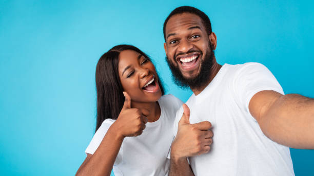 istock Happy afro couple taking selfie gesturing thumbs up and smiling 1325279656