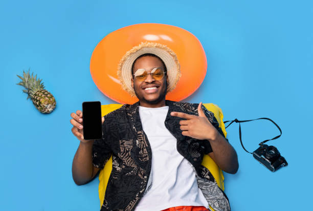 istock Top view of cool black guy lying on inflatable lilo, pointing at smartphone with blank screen, mockup for mobile app 1325279700