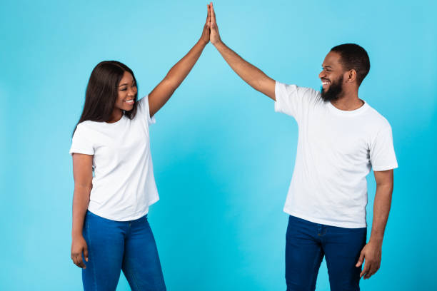 Portrait of happy black couple celebrating win giving high five Couple Teamwork Concept. Portrait Of Joyful African American Guy And Lady Giving High Five, Looking At Each Other, Celebrating Success And Triumph, Standing Isolated Over Blue Studio Background couple hope sky blue stock pictures, royalty-free photos & images