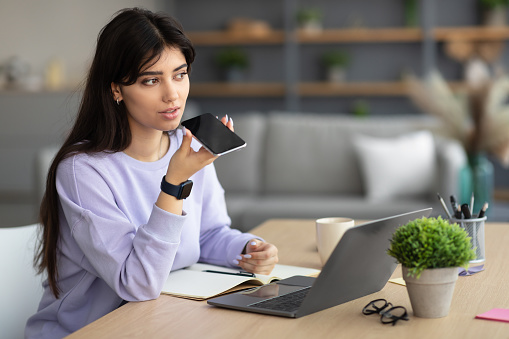 Work From Home. Portrait Of Young Business Lady Using Voice Search Assistant, Talking On Mobile Phone And Using Laptop Computer. Woman Sitting At Desk With Pc At Home Office, Free Copy Space