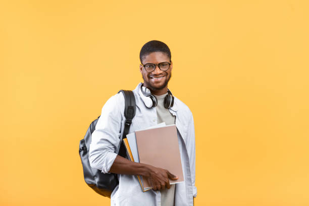 istock Education concept. Excited african american guy with backpack, headphones and notebooks posing on yellow background 1325280606