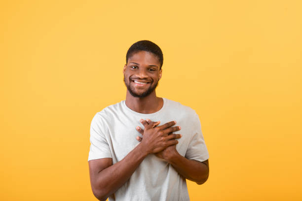 istock Pleased guy keeping palms on heart, feeling hope and love over yellow background, studio shot 1325282009