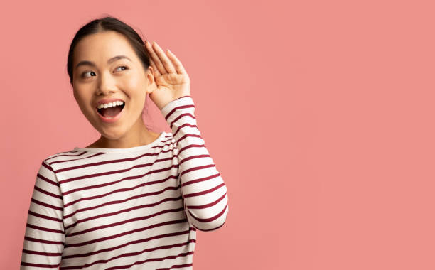 Curious cheerful asian woman keeping hand near ear trying to overhear something Curious cheerful asian woman keeping hand near ear trying to overhear something, interested young korean lady eavesdropping and enjoying gossips, standing isolated over pink background, copy space beckoning photos stock pictures, royalty-free photos & images