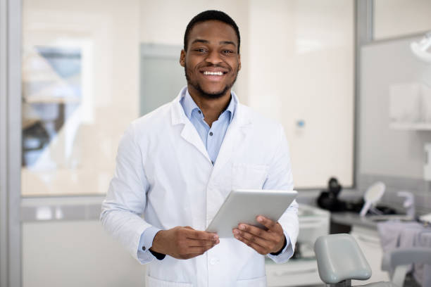 ritratto di sorridente bel dentista nero medico con tablet digitale in mano - dentista foto e immagini stock