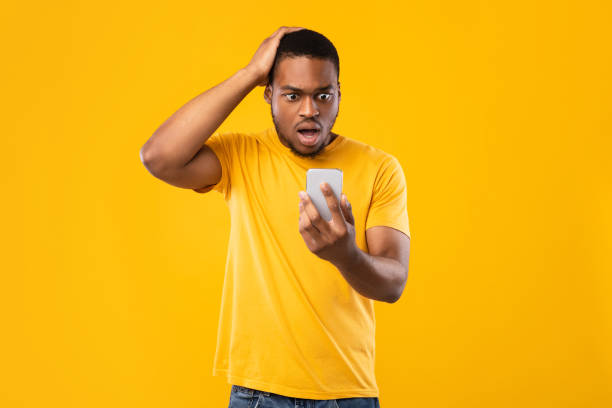 istock Concerned Black Guy Looking At Cellphone In Shock, Yellow Background 1325282084