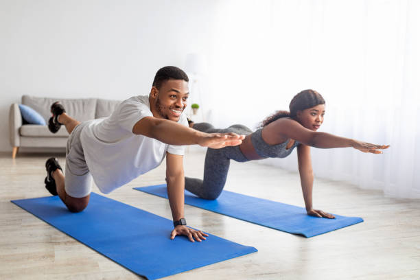 pareja negra en forma estirando los brazos y las piernas, haciendo yoga o pilates en colchoneta en interiores. quédate en casa aficiones - stretching boyfriend indoors lifestyles fotografías e imágenes de stock