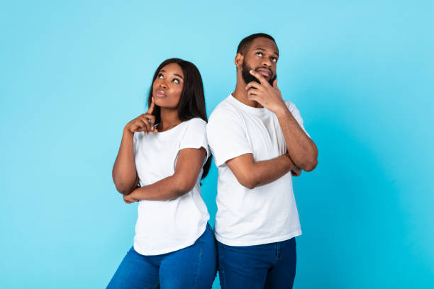 Black man and woman thinking on blue background Portrait of thoughtful black guy and lady thinking about question and looking up, touching chin, planning future vacation and making decision, standing back to back on blue color studio wall men hairstyle afro cool stock pictures, royalty-free photos & images